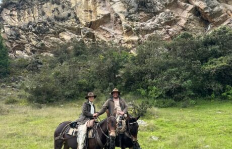 Dos jinetes en mula frente a un farallón de roca en la cabalgata Suesca – Nemocón, Suesca